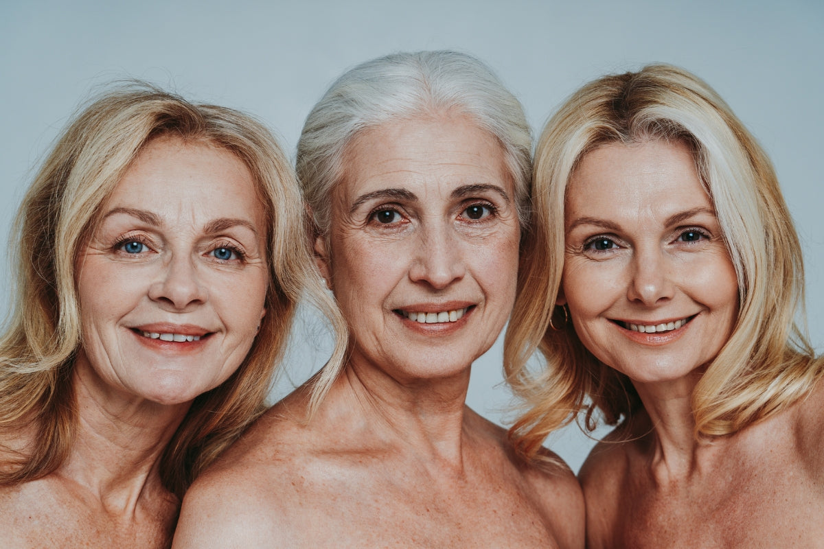 3 ladies, 2 blonde and one white haired, are all standing close together smiling into the camera.