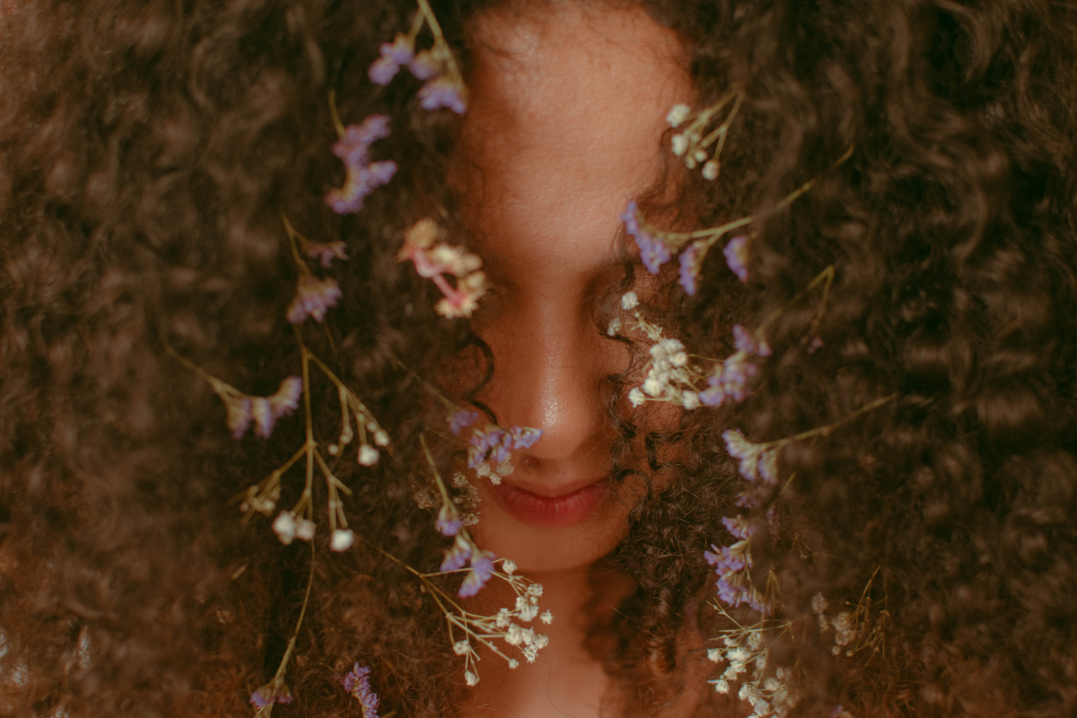 Brown long curly hair with flowers through the front of her hair.