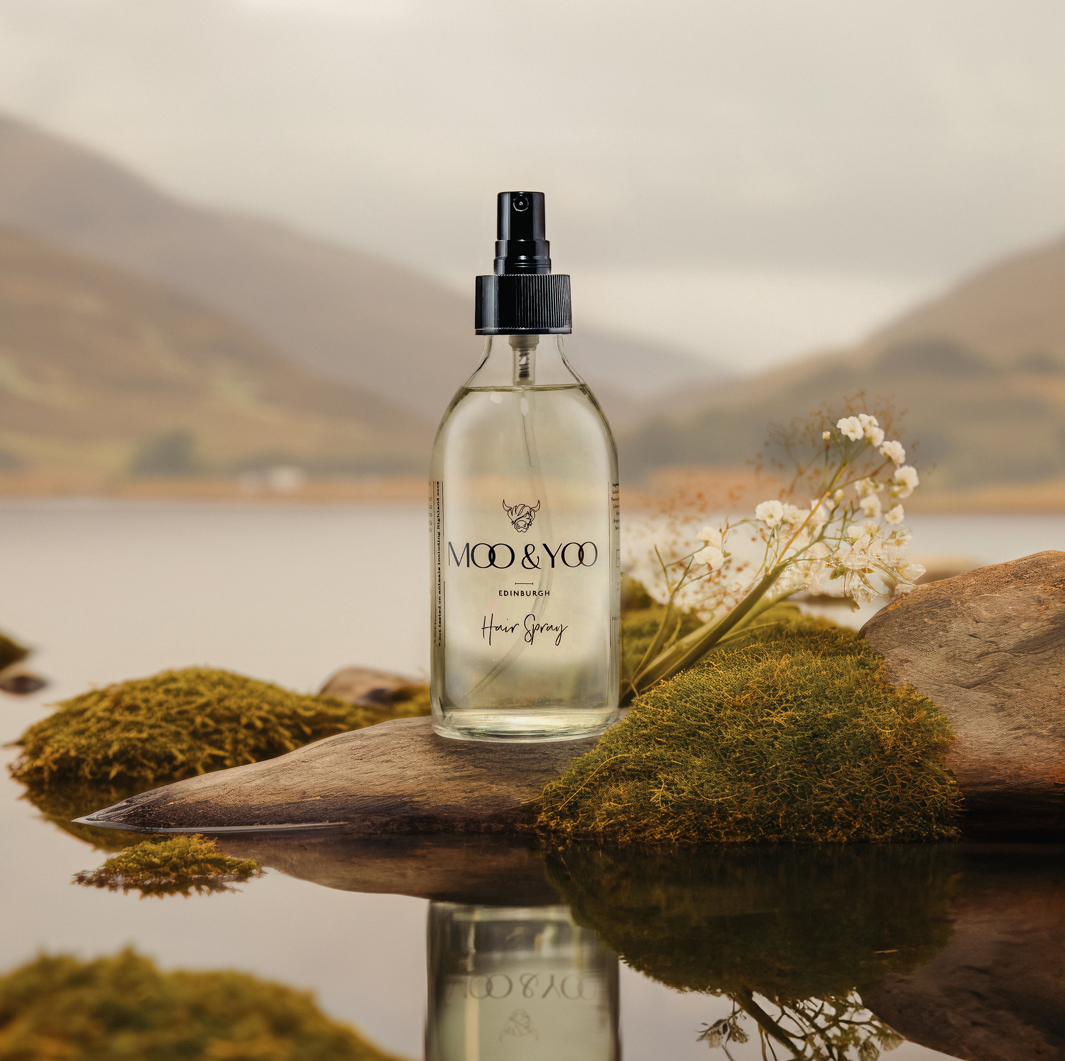 Our hair spray in a glass bottle on a small rock peaking out onto the loch with the water surrounding it and munros in the background