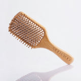 A bamboo paddle brush with natural rubber pins, lying on a white surface.