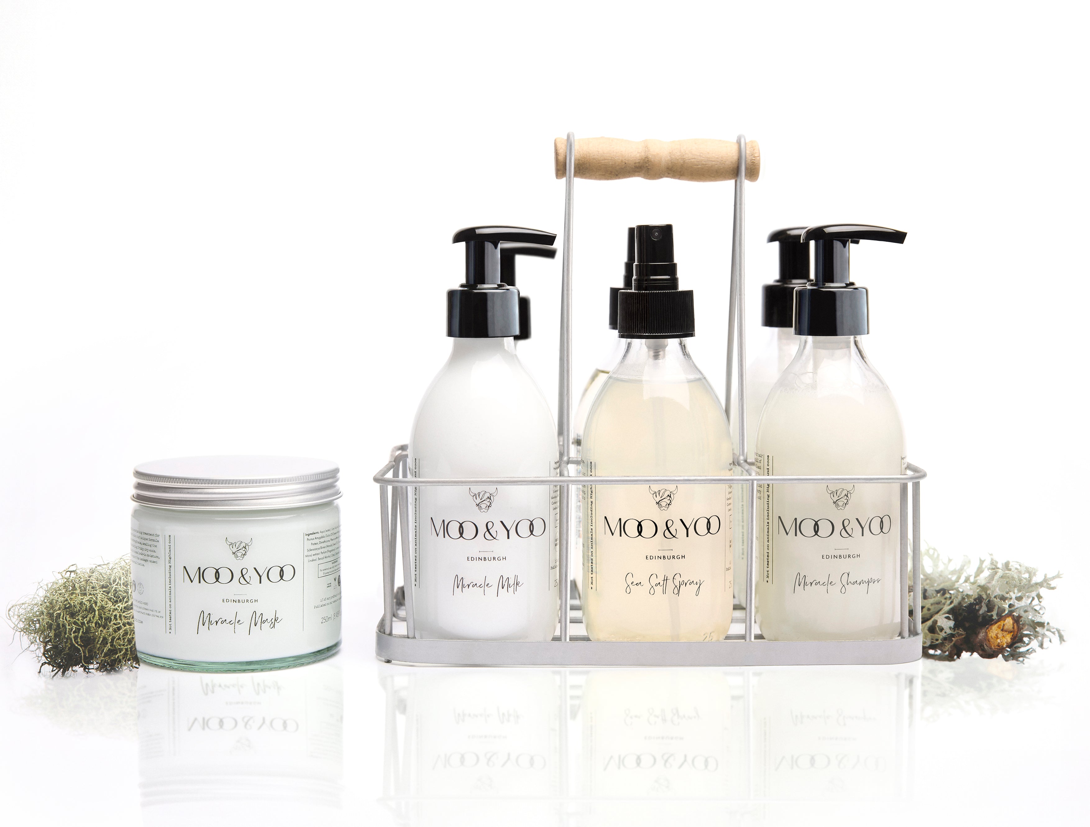 studio photo of moo & yoo product carrier caddy crate with bottled moo & yoo products in the crate ansd a jar of miracle mask to the left of the caddy. There is a white background and pieces of moss at the side of the products