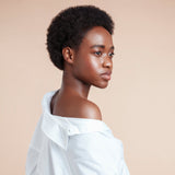 Female model with black natural textured hair from using Moo and Yoo Miracle Mask, Miracle Milk and Miracle Curl Cream. She is wearing an off the shoulder white shirt and is facing the back looking over her shoulder to the side