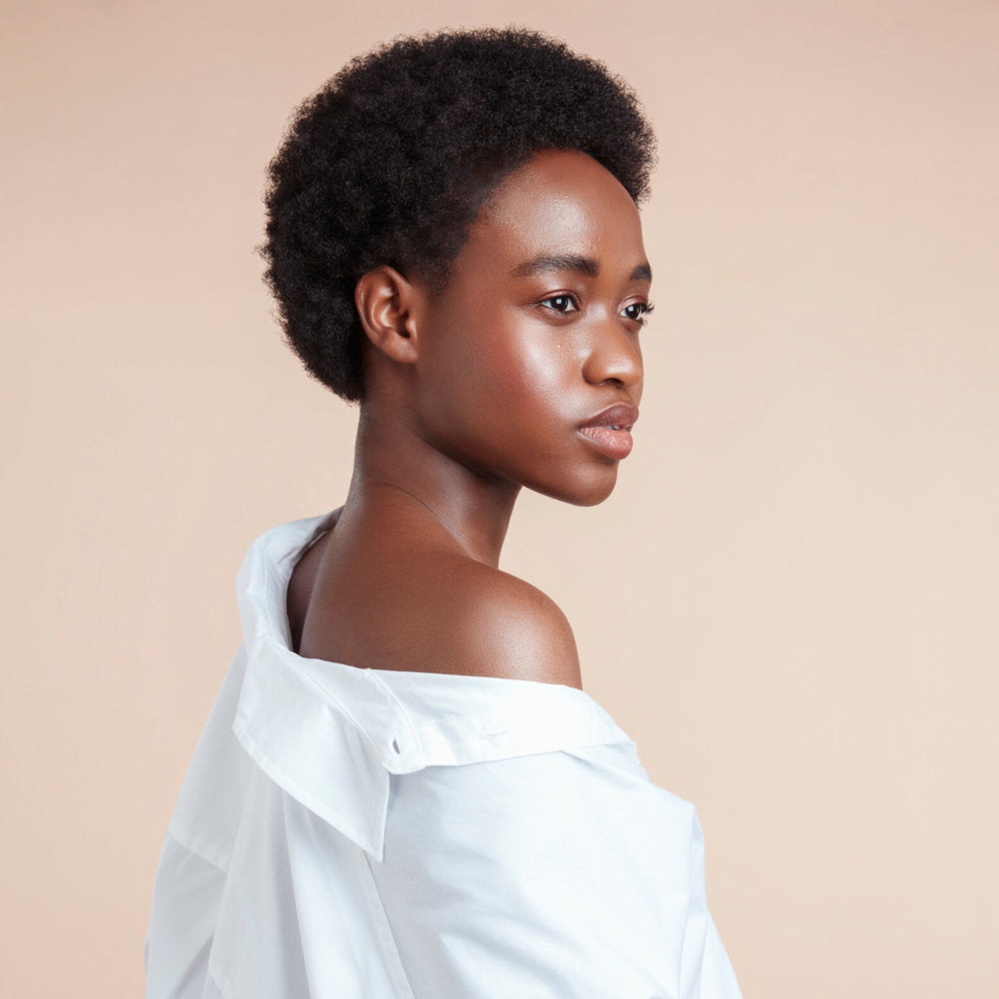 Female model with black natural textured hair from using Moo and Yoo Miracle Mask, Miracle Milk and Miracle Curl Cream. She is wearing an off the shoulder white shirt and is facing the back looking over her shoulder to the side