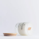 Glass jar with bamboo lid of Moo and Yoo signature scent luxury vegan candle. It is on its side showing the wooden wick with the lid to the side and on a white backgroun d.
