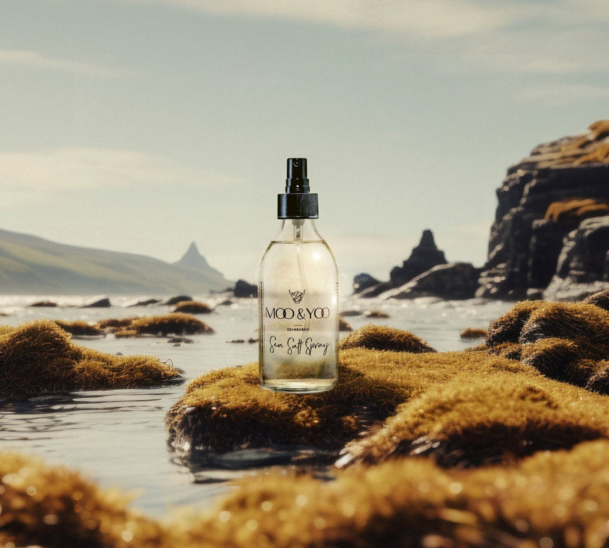 A glass bottle of Moo and Yoo Sea Salt Spray sitting on a mossy rock at the edge of a Scottish Loch