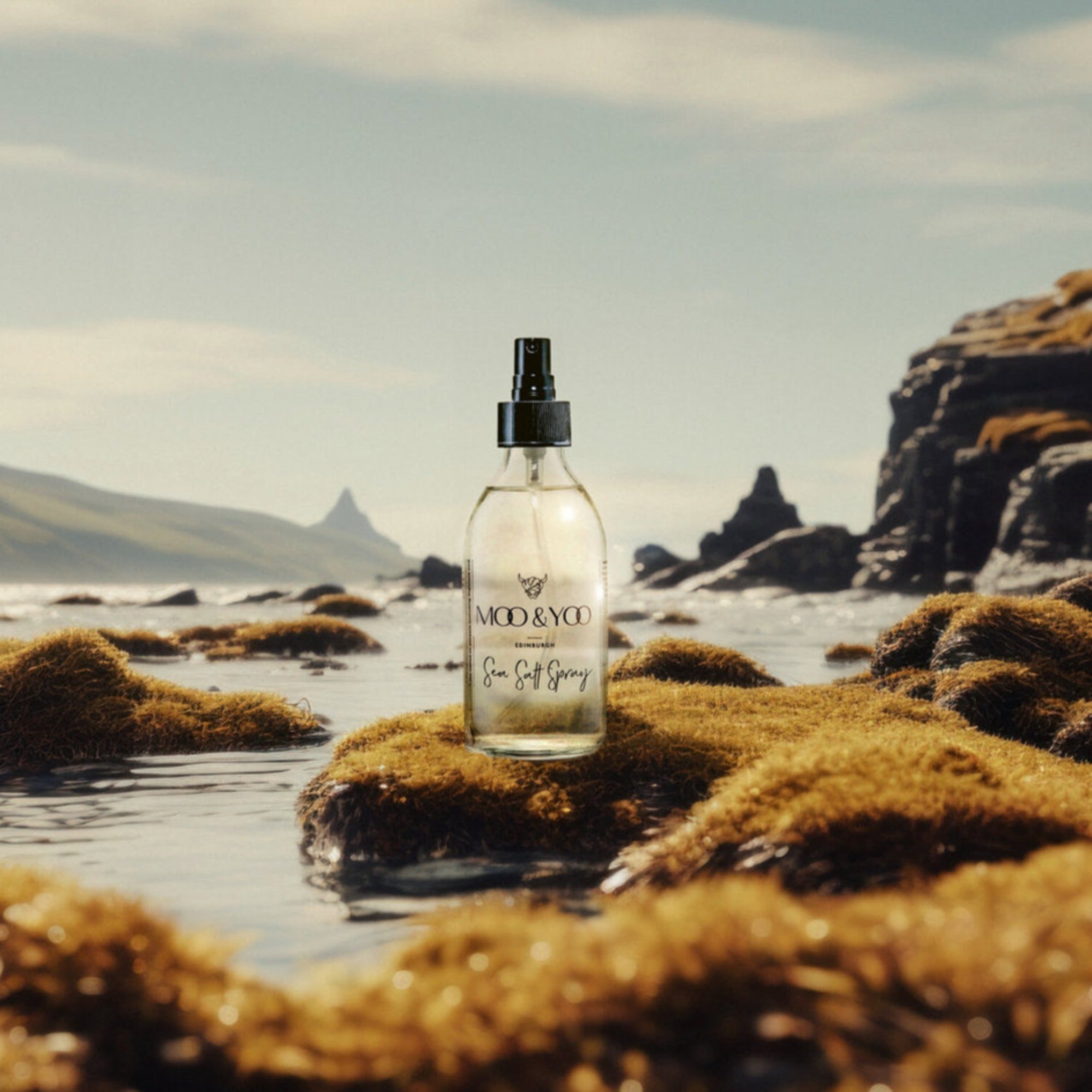A glass bottle of Moo and Yoo Sea Salt Spray sitting on a mossy rock at the edge of a Scottish Loch