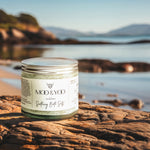 Jar of 'Moo & Yoo' bath salts on a rock with a scenic background at the beach