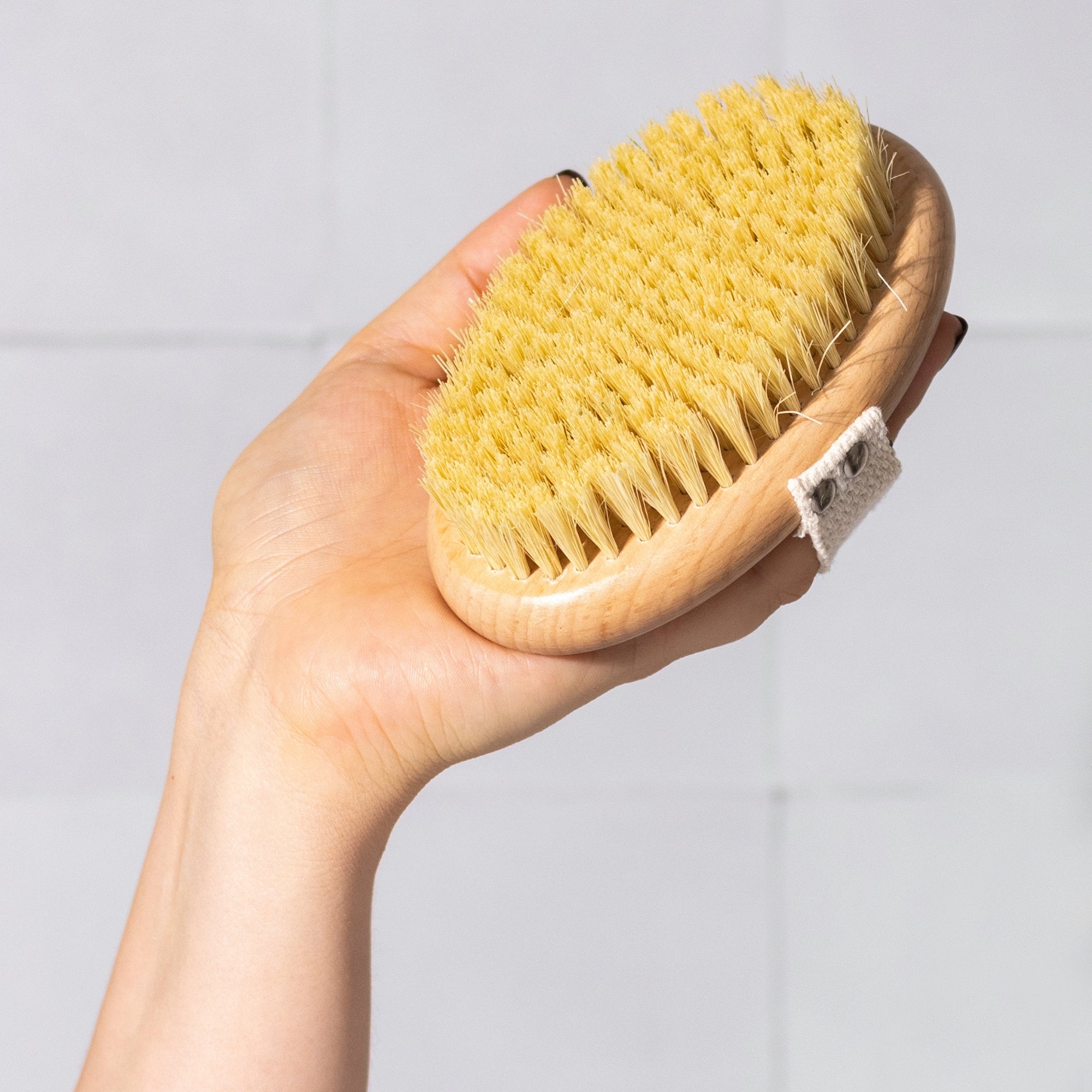 Hand holding a natural bristle brush against a white tile bathroom background