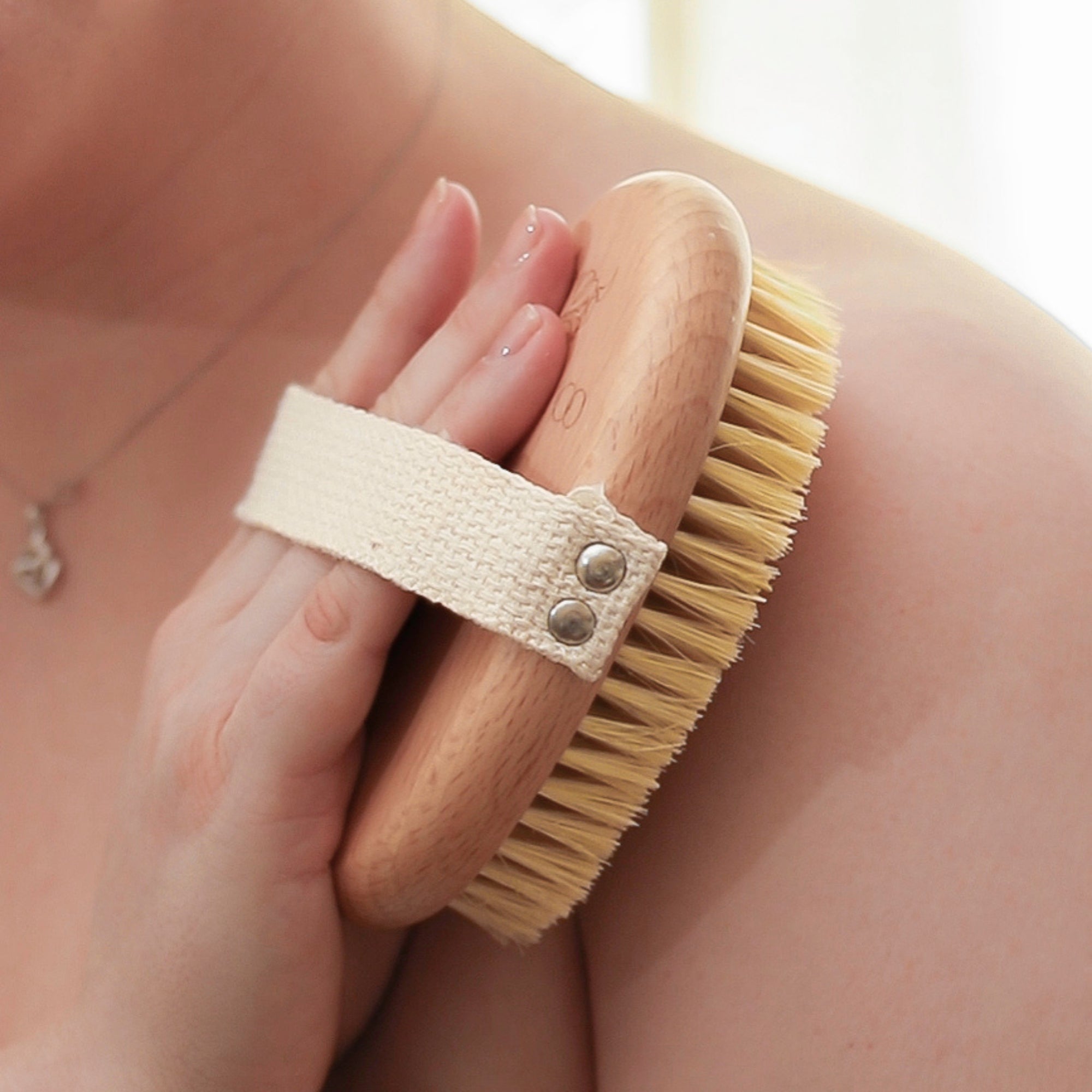 Person using a wooden body brush with natural bristles on their shoulder.