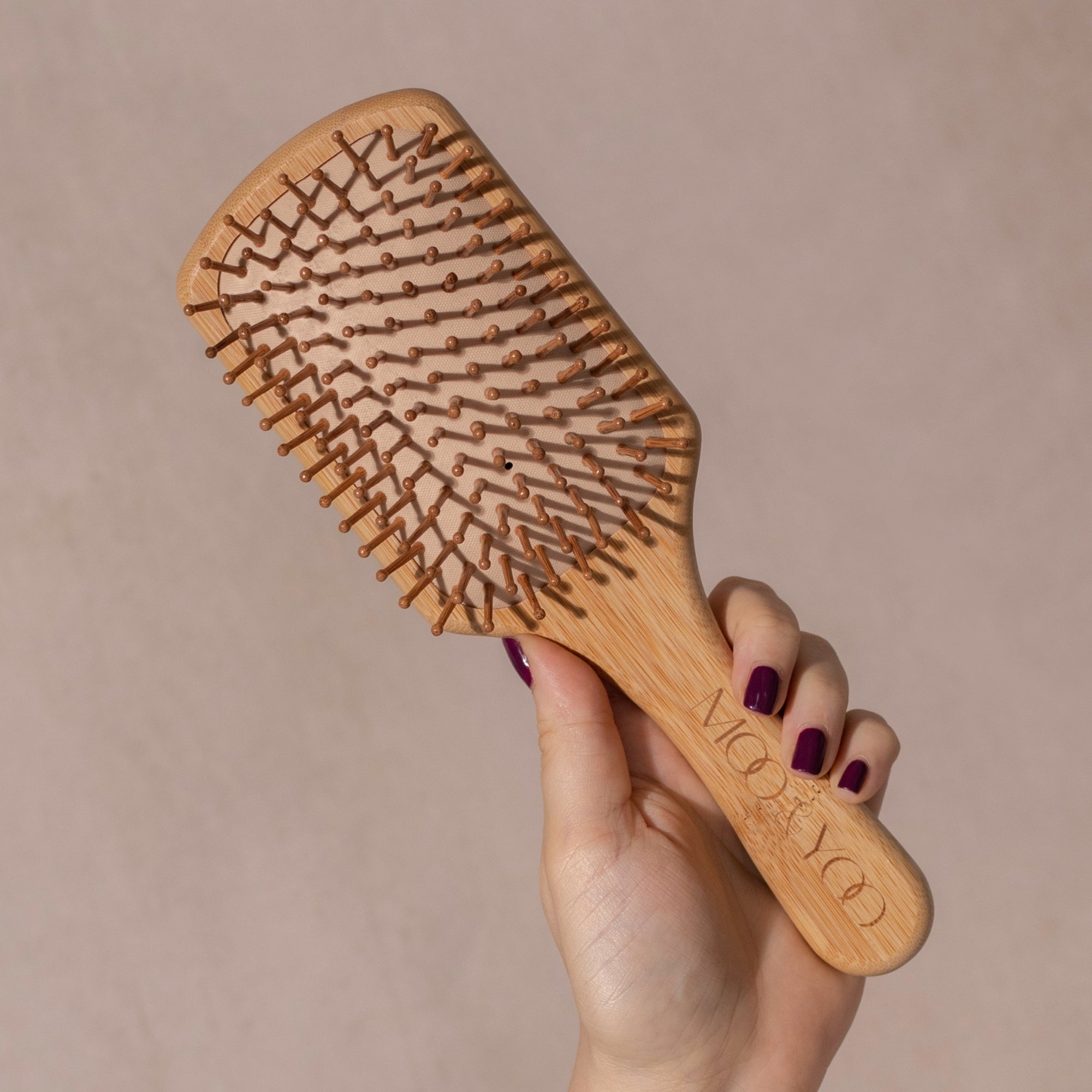 Wooden hairbrush held by a hand with a neutral background