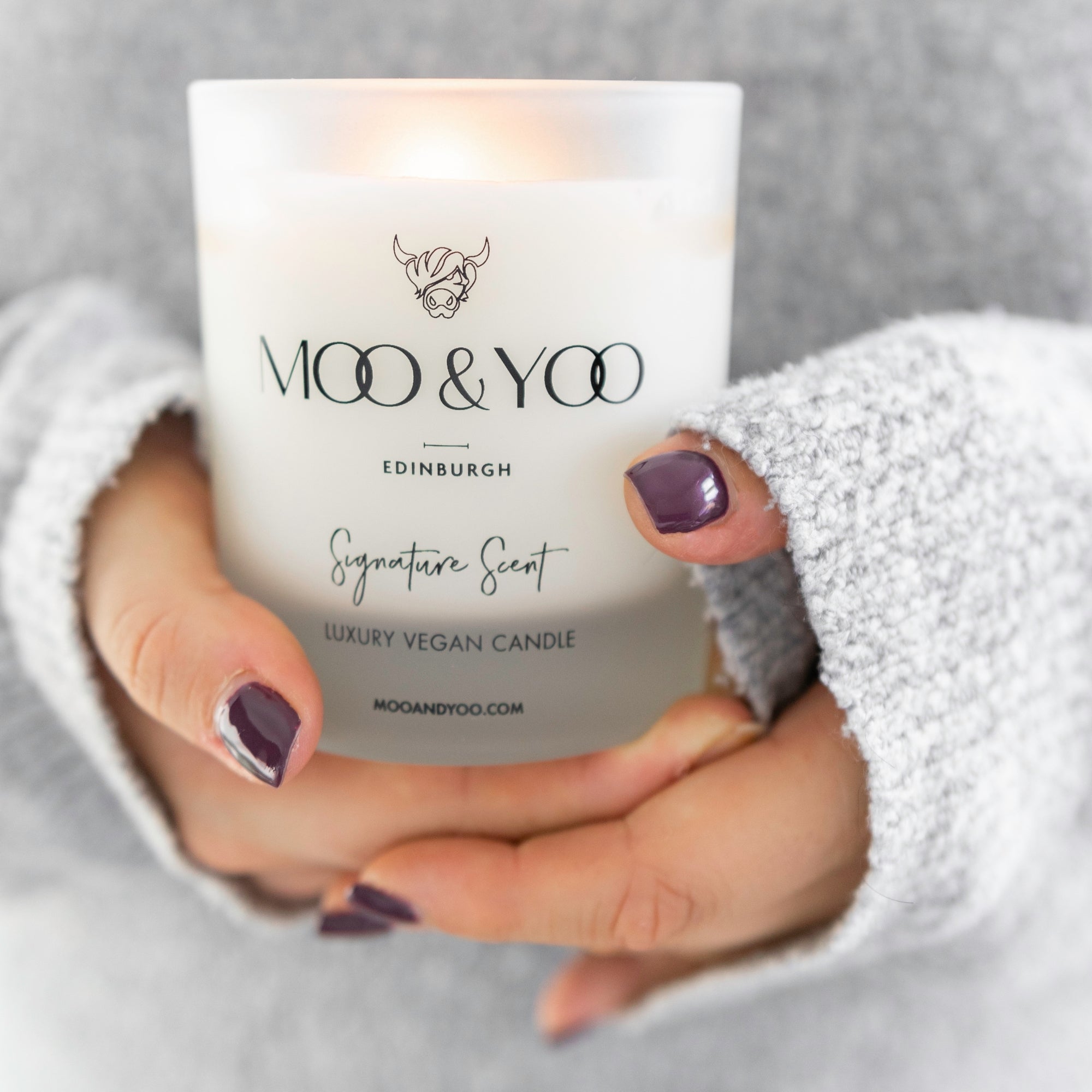 Person holding a 'Moo & Yoo' candle infront of them wearing a grey jumper