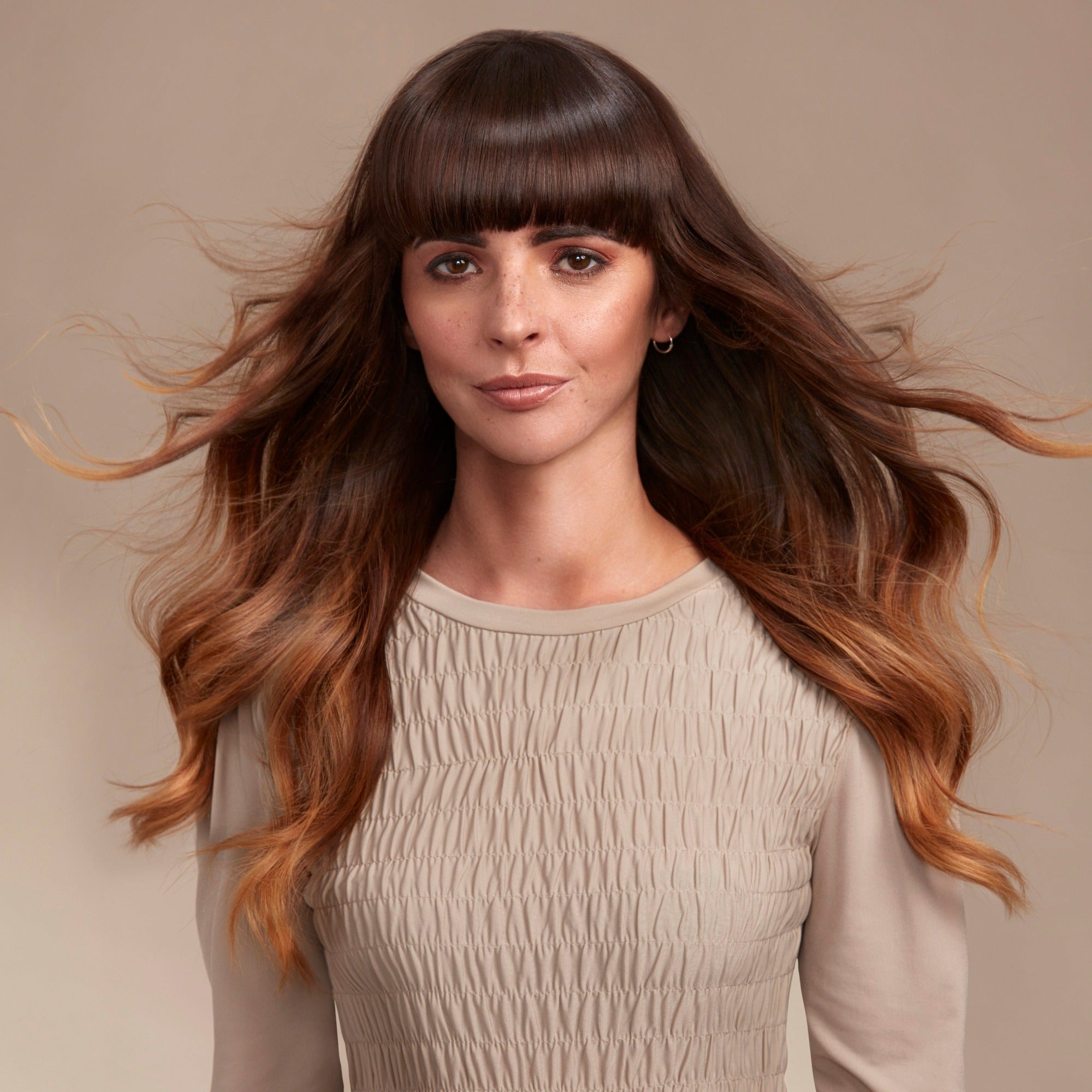 Female model with long flowing brunette hair. She has super shiny hair with lots of volume from Moo and Yoo Shampoo and Conditioner and Volumising Spray Mist. She is looking directly at the camera and is wearing a neutral coloured top