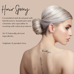 Woman with platinum blond hair styled in a low bun with her back to the camera facing the side displaying her tattoos on a beige background, promoting a hair spray product.