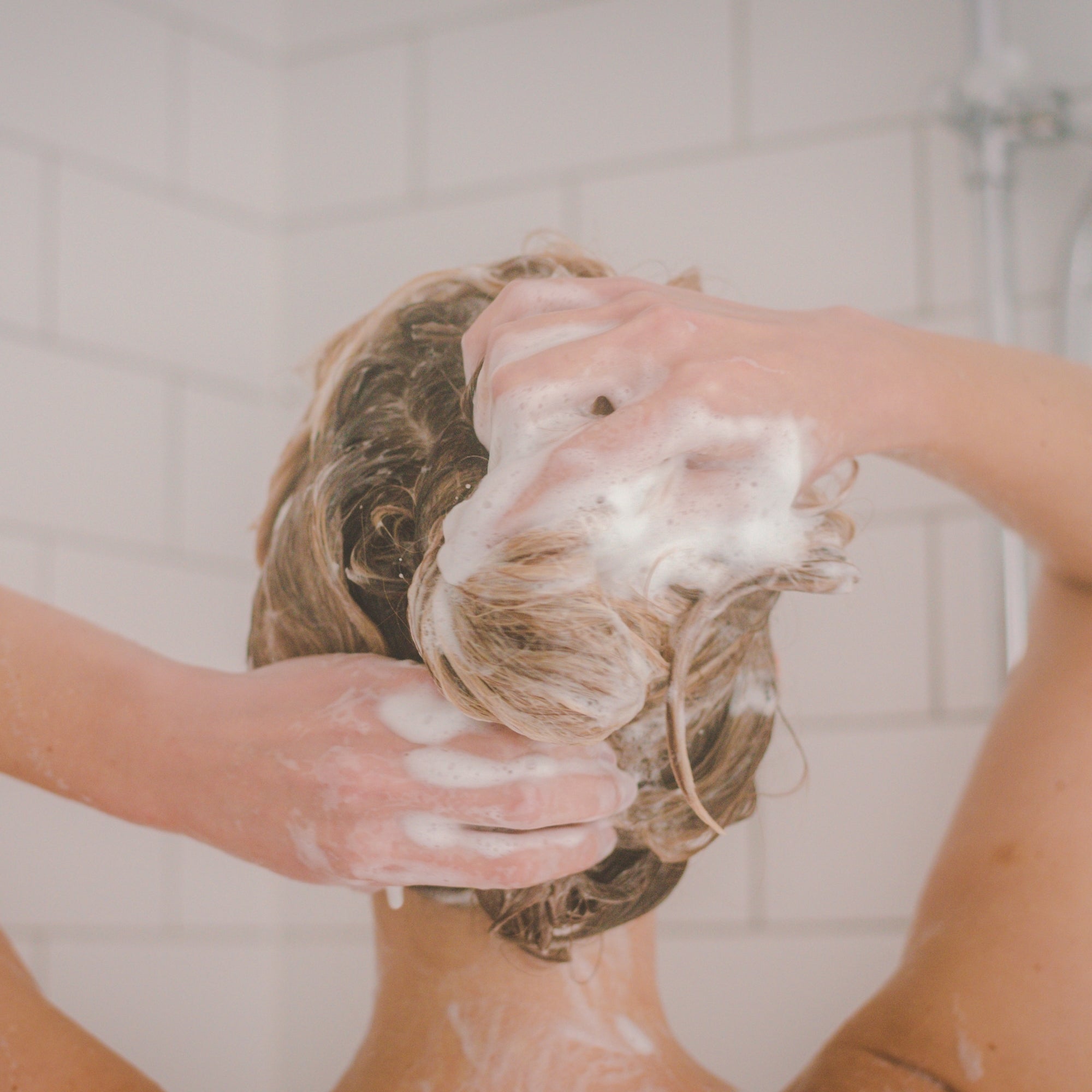 Person washing her hair with moo & yoo miracle shampoo in a bathroom setting
