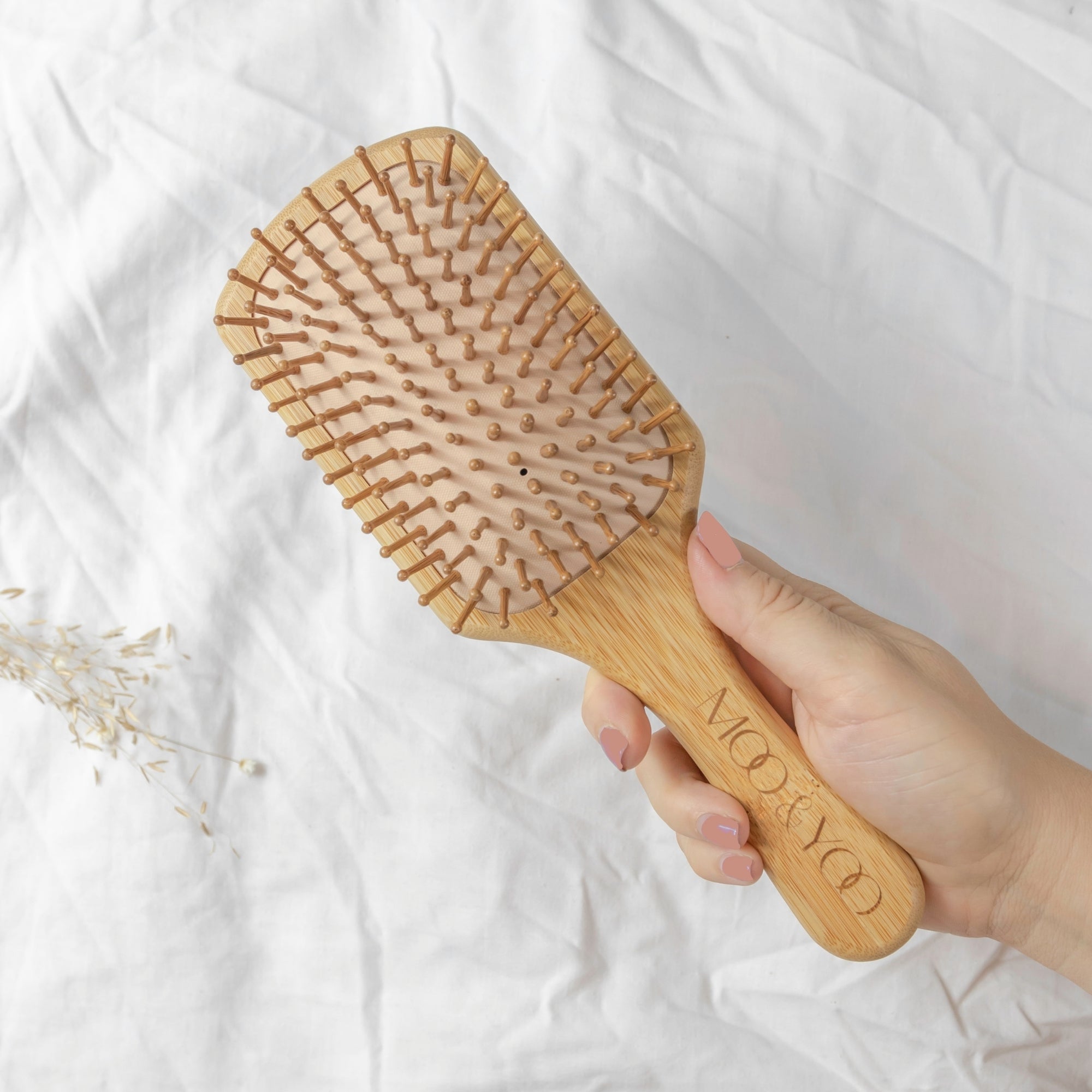 Wooden hairbrush held by a hand on a white sheet background