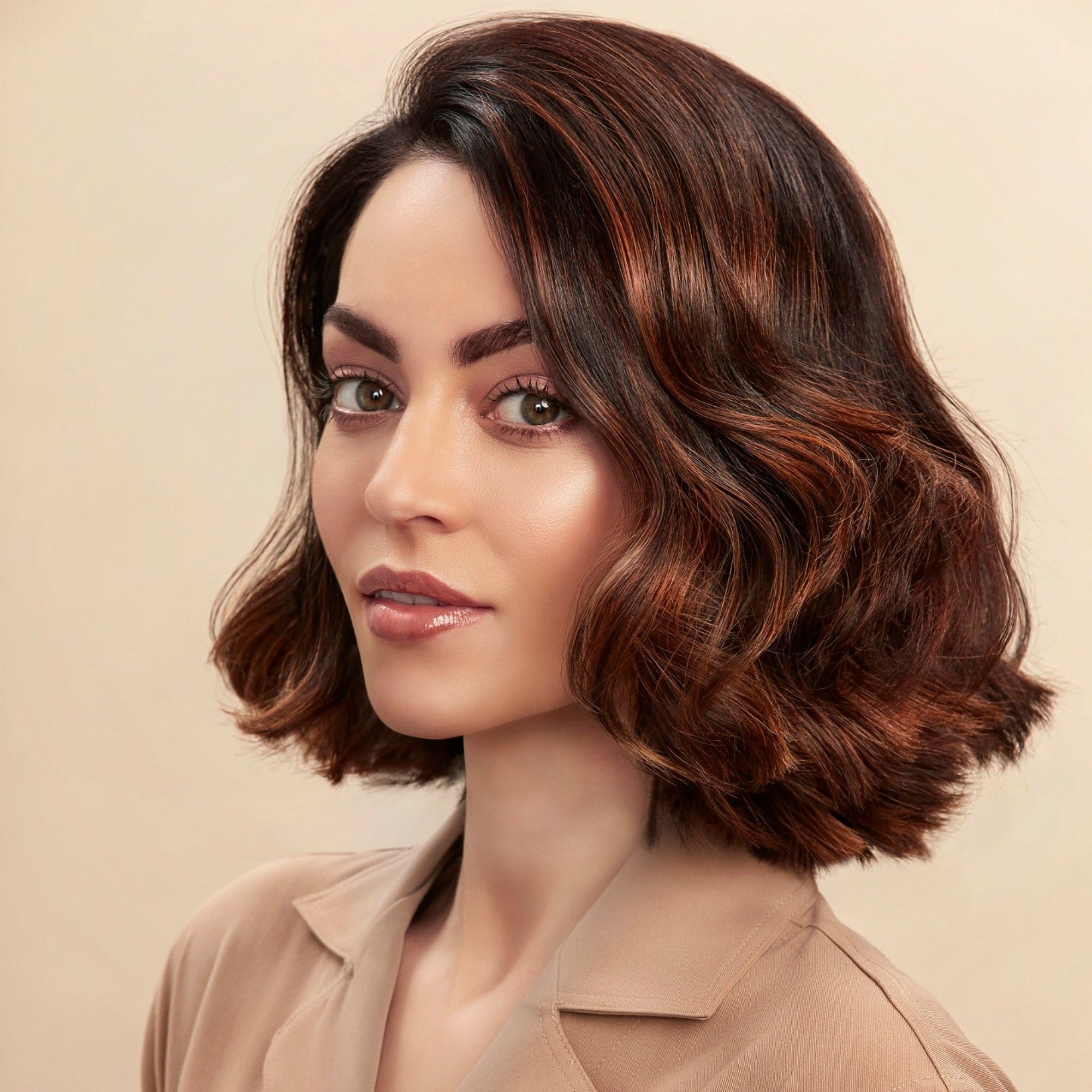 Female model with a wavy bob and brunette hair. She has super shiny hair and has used Moo & Yoo Miracle Shampoo, Conditioner and Volumising Spray Mist so she has lots of volume. She is looking at the camera from a side angle and is wearing a neutral coloured shirt.