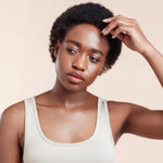 Woman with natural cropped afro hair wearing a white tank top against a beige background