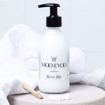 Bottle of Moo & Yoo Miracle Milk with a pump on a white linen platform and a white fluffy towel in the background