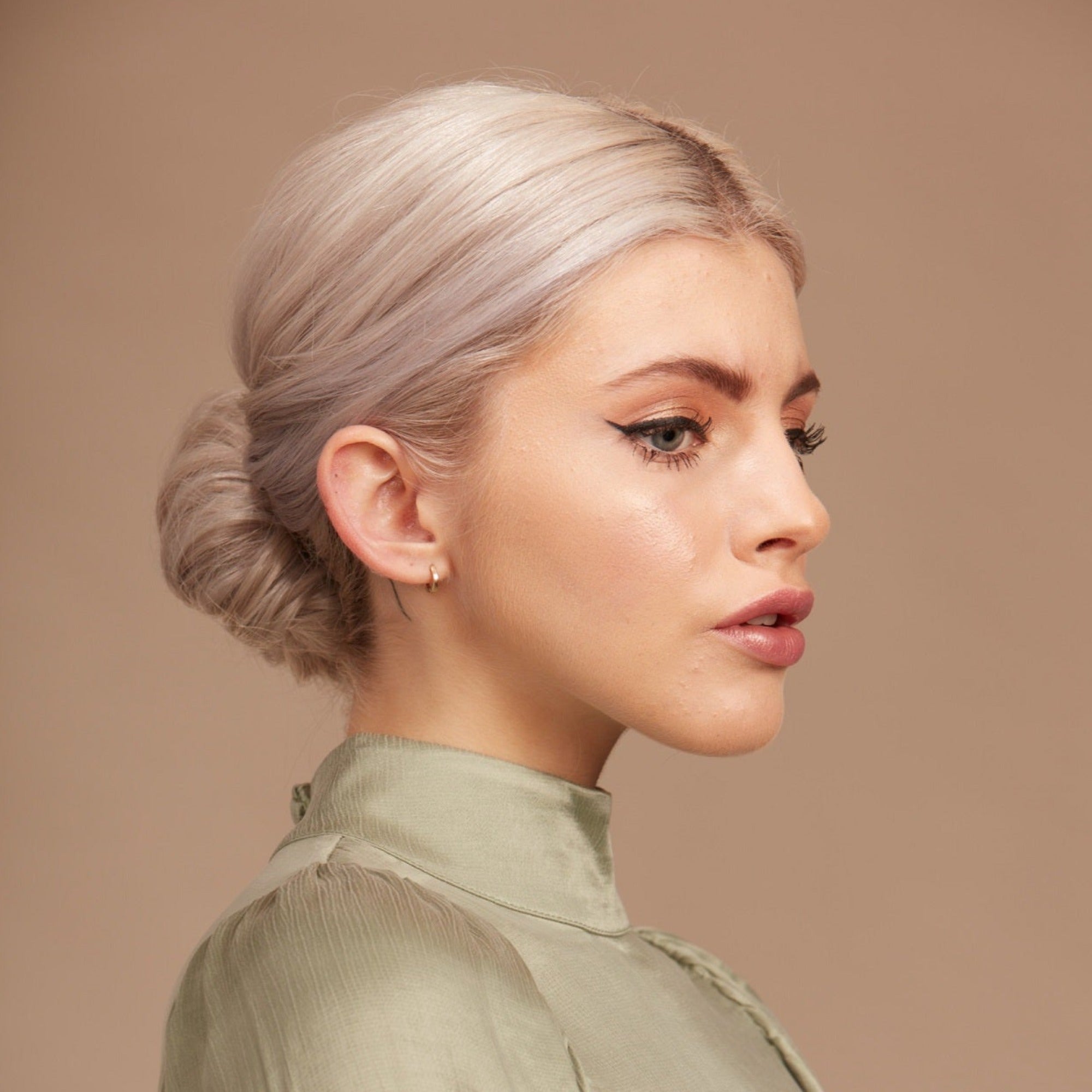 Female model with bleached blond hair in a low bun. She has processed hair so has used Moo and Yoo Miracle Conditioner and Mask.  She is facing side on and looking to the right. She has on a pale green silk high neck top