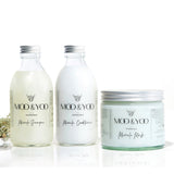 Two glass bottles and a glass jar of Moo and Yoo products sitting side by side. It is a Miracle Shampoo, Conditioner and a Miracle mask. They all have aluminium lids. They are on a white background with a sprig of Icelandic moss placed to one side.