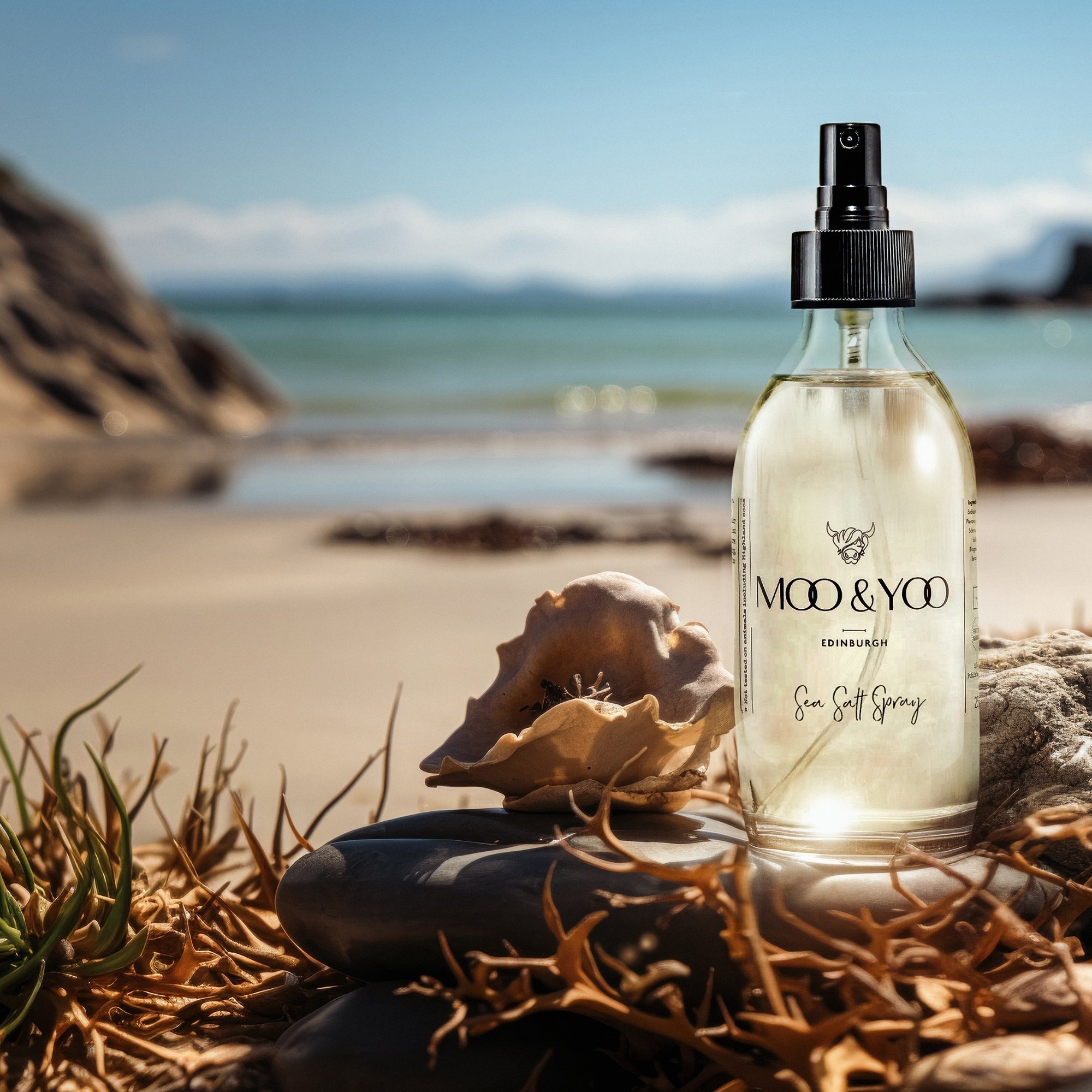 Moo & Yoo Sea Salt Spray bottle on a beach with shells and rocks.