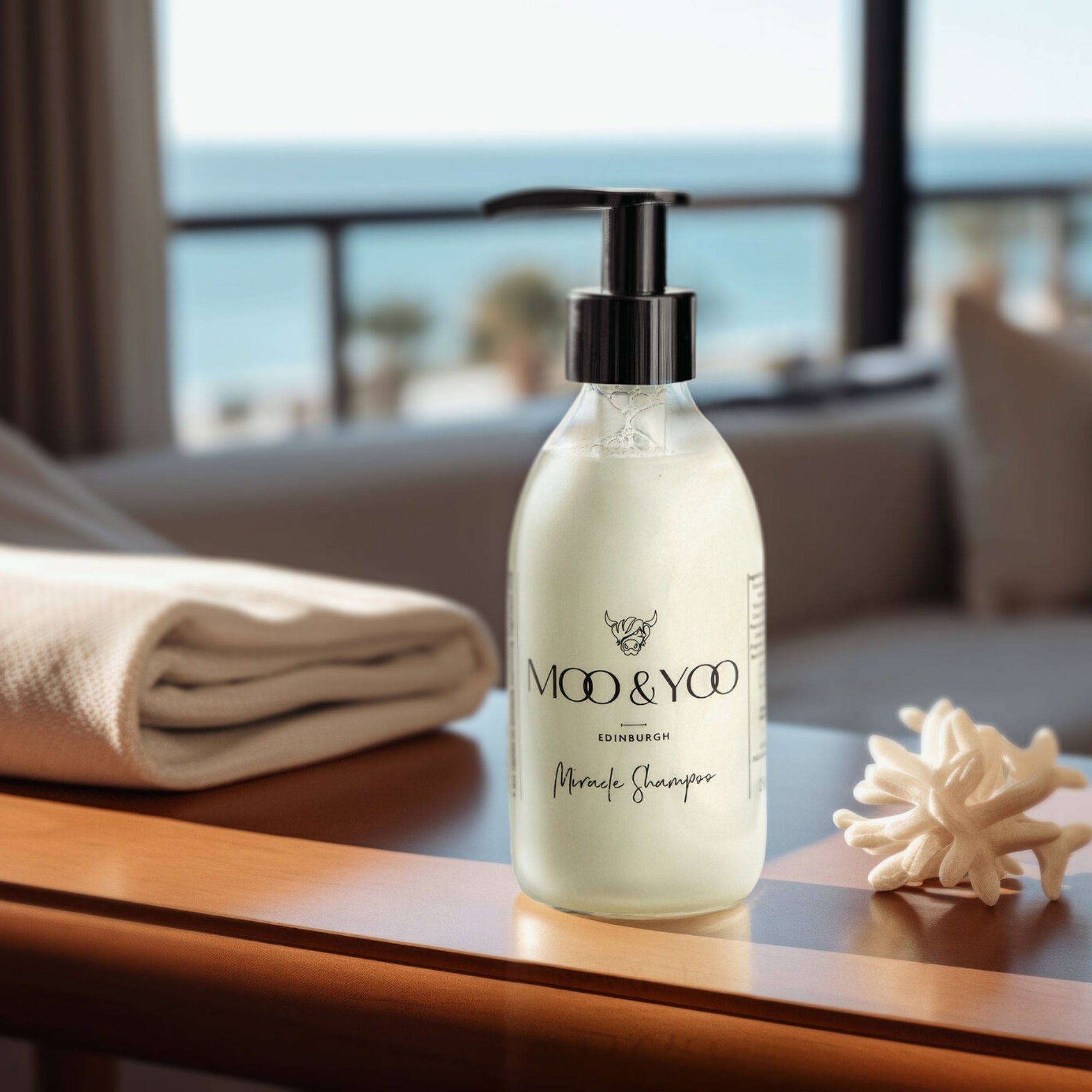 Moo & Yoo shampoo bottle on a table with a blurred beach background