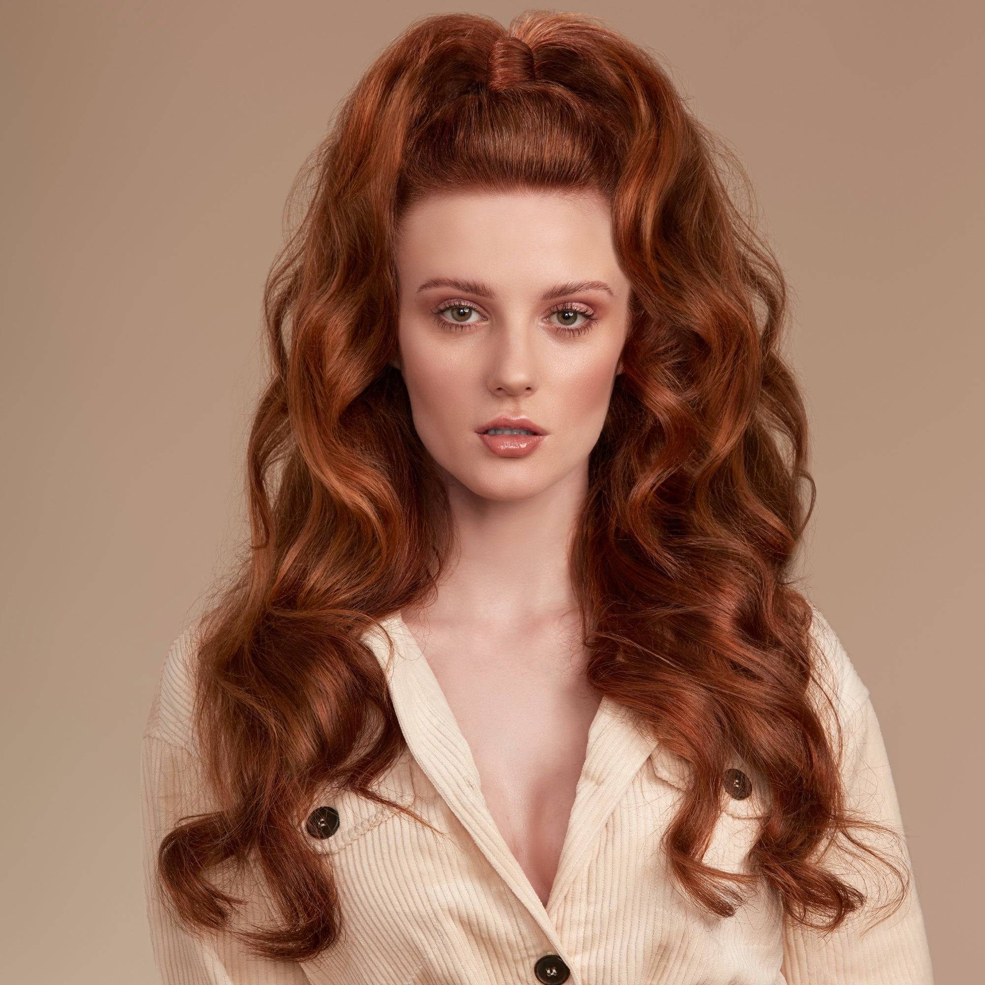 Woman with long, wavy red hair wearing a light-colored blouse against a beige background