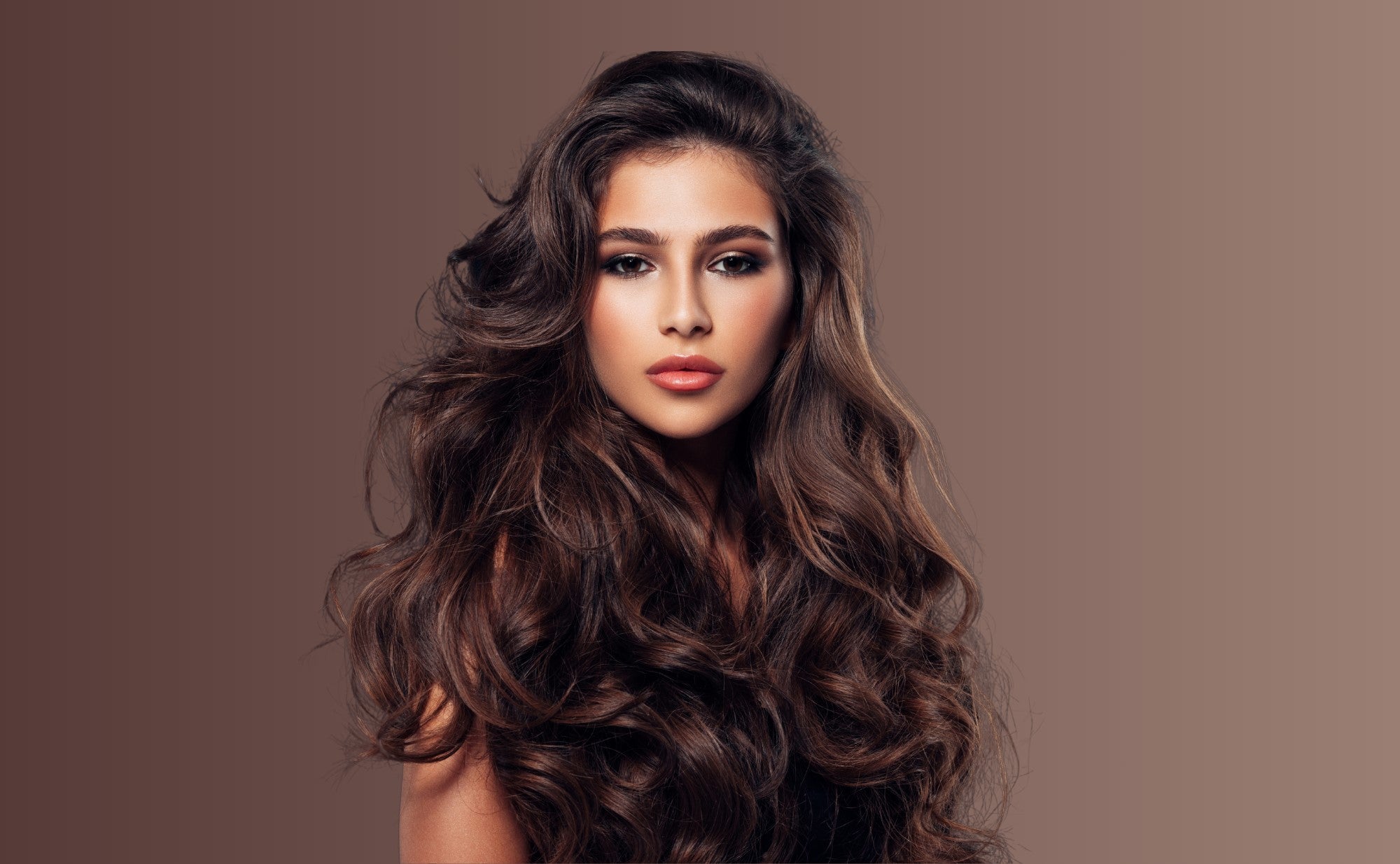 Female model with long, glossy, type 2C hair looking at the camera against a brown background.