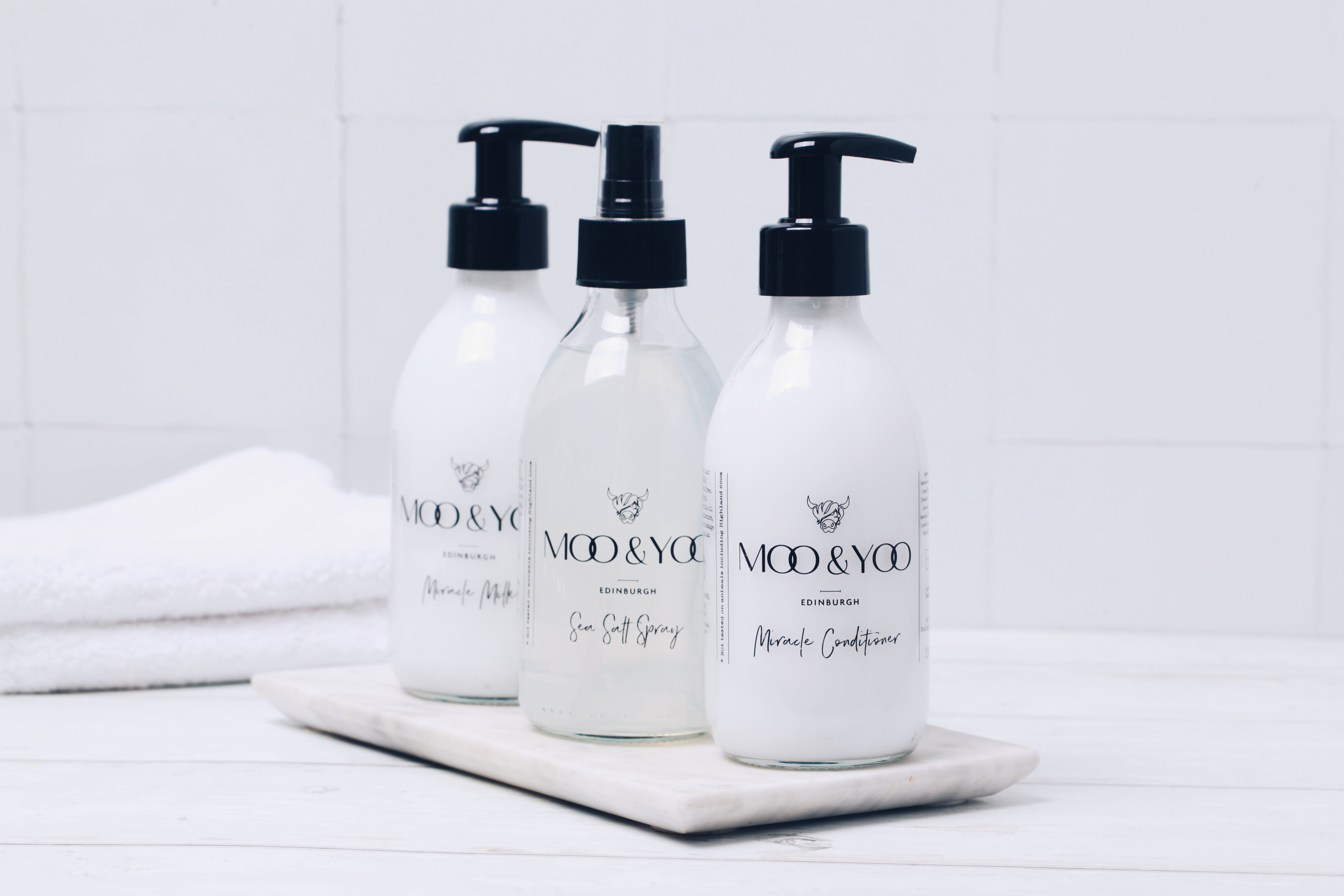 4 Moo & Yoo products are lined up next to each other. there is a white background behind them and there is some moss placed in between each bottle.