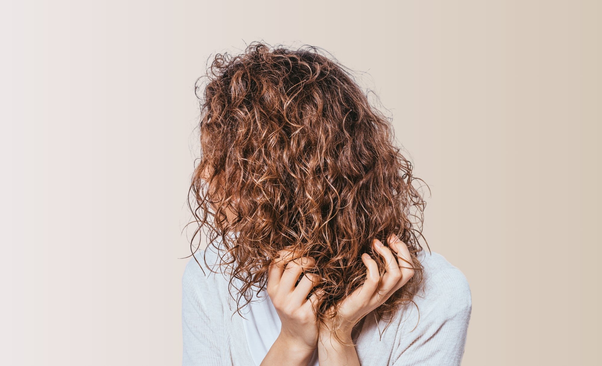 A girl scrunching her type 3a hair towards the camera against a light beige background.