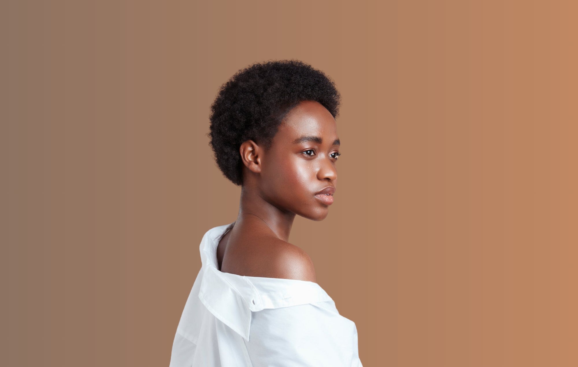 Girl looking over her shoulder with Type 4C hair, in front of a beige background.