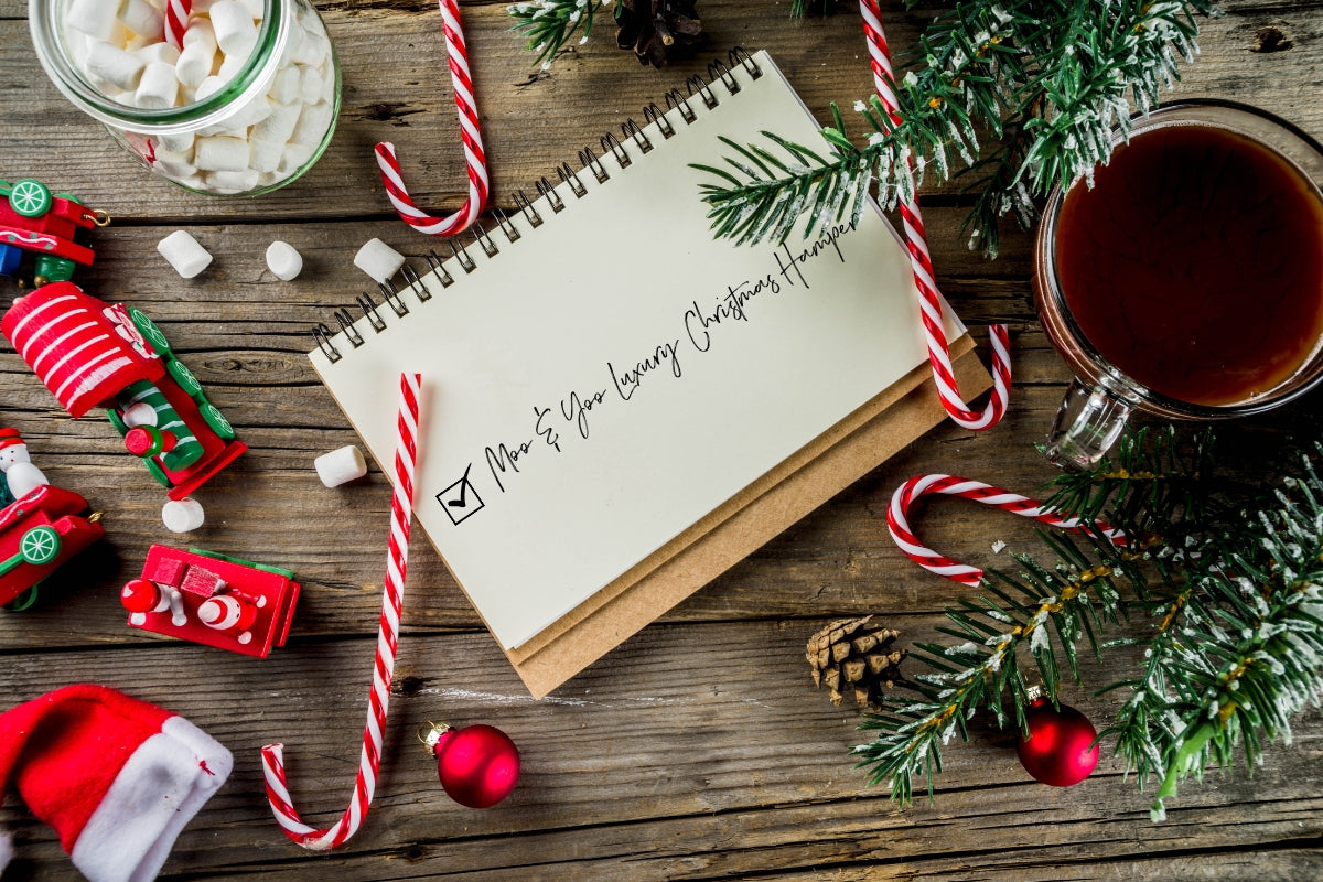 Festive decorated table with a christmas list that says 'Moo & Yoo Luxury Christmas Hamper' on it.