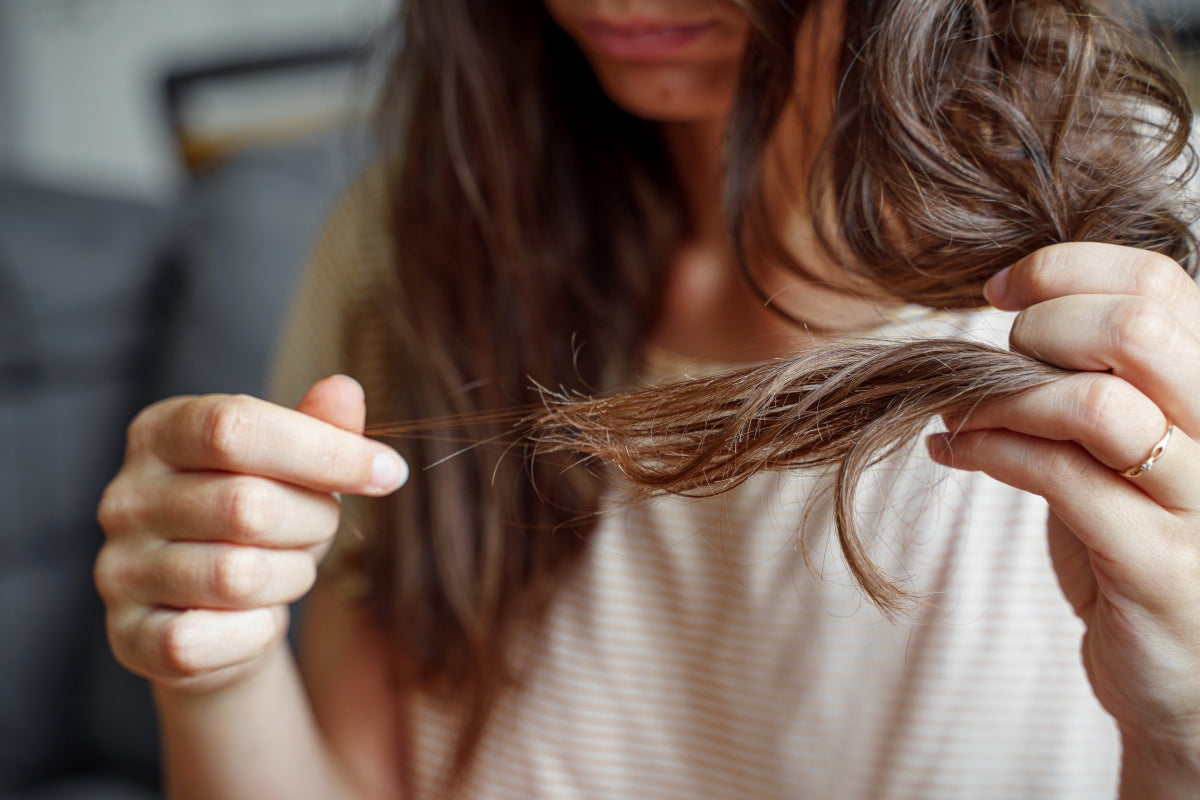 A close up image of a woman inspecting the ends of her hair.