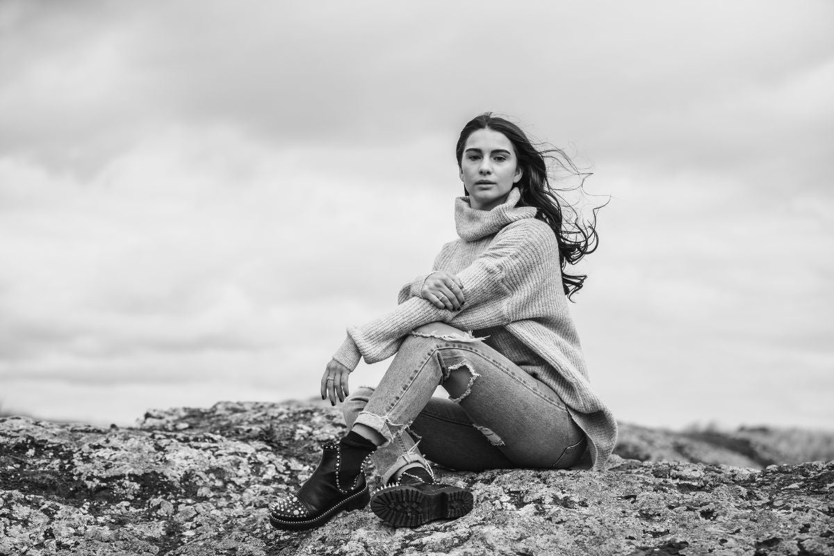 Black and white image of a model sitting on a big rock outdoors with her hair flowing in the wind.