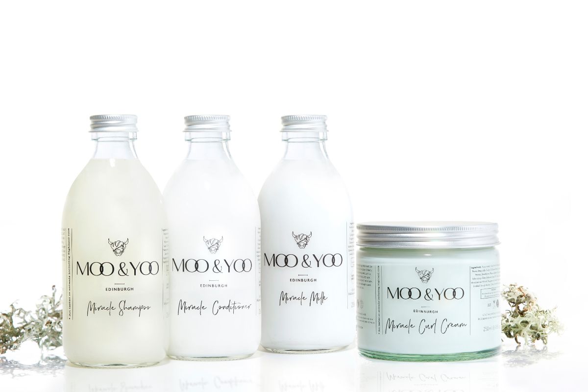 4 Moo & Yoo products (shampoo, conditioner, milk and mask) are all lined up infront of a wehite background with some moss on either side of the products.