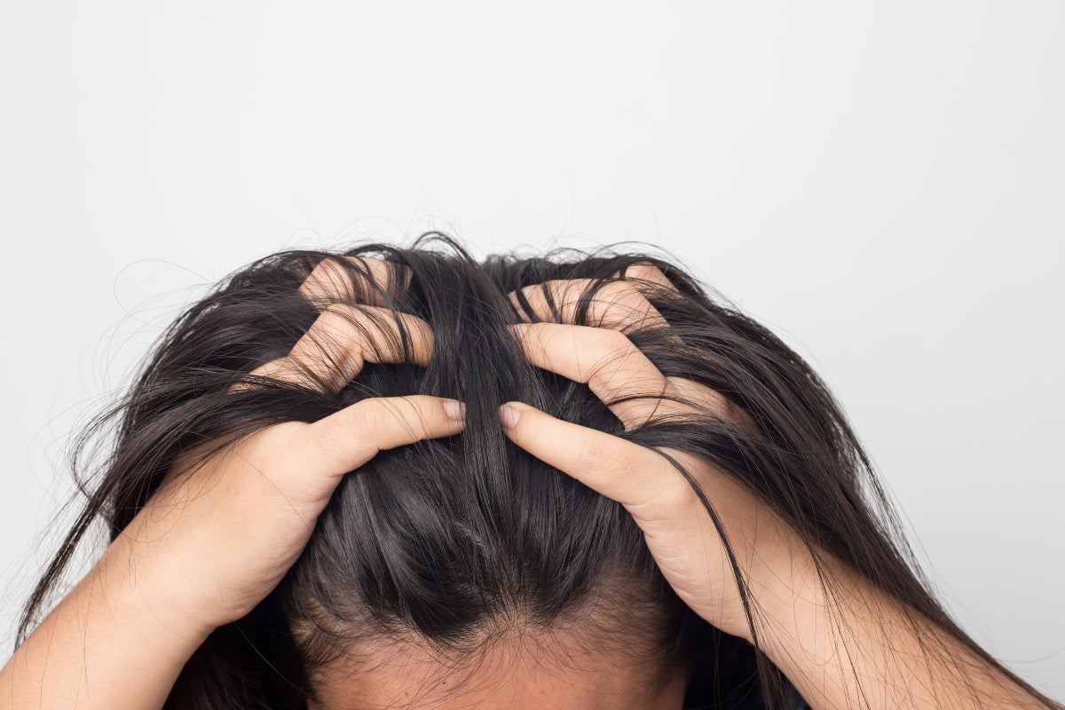 This image shows hands running through some dark brown hair. This is a landscape image and you can only see the persons forehead and hair.