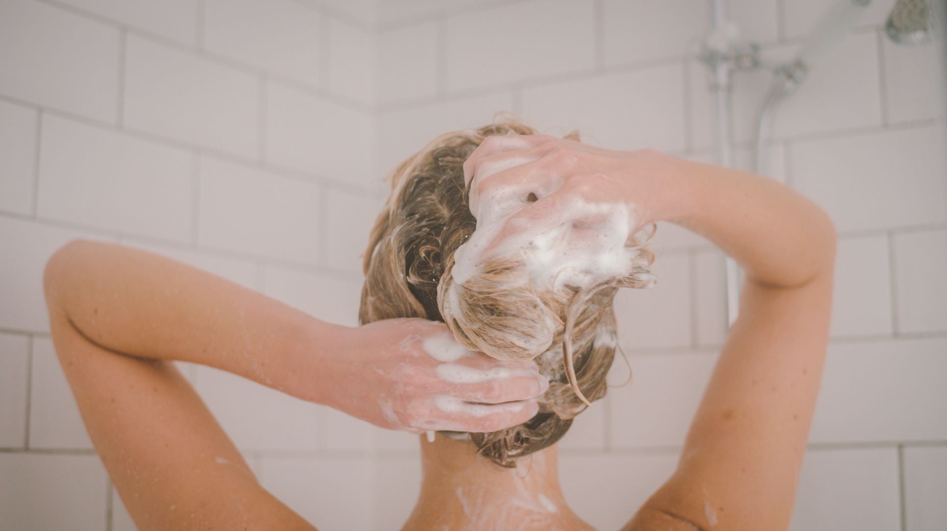 miracle shampoo being used as girl is in the shower lathering her hair with white tile background