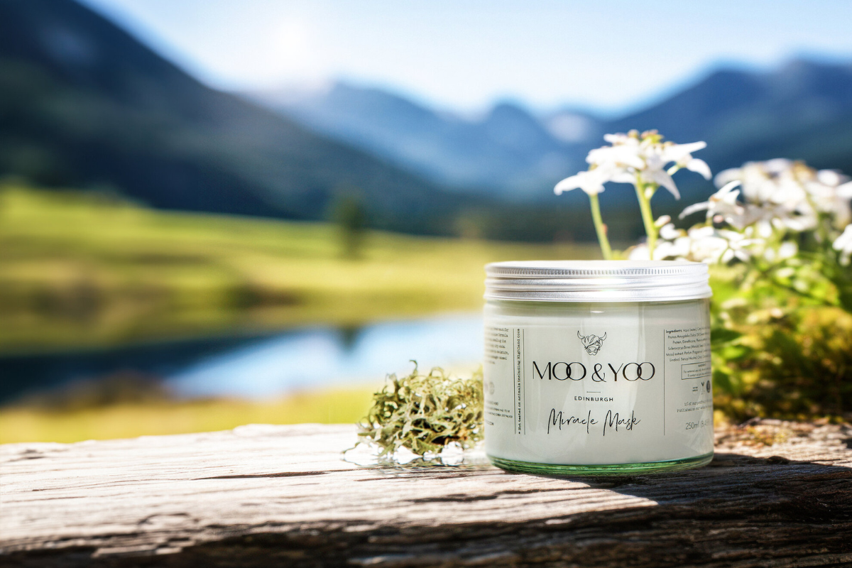 A Moo & Yoo Miracle Mask is placed on a peace of wood in front of a beautiful Scottish loch and moutains. The background is blurred with the Miracle Mask as the main focus on this image.