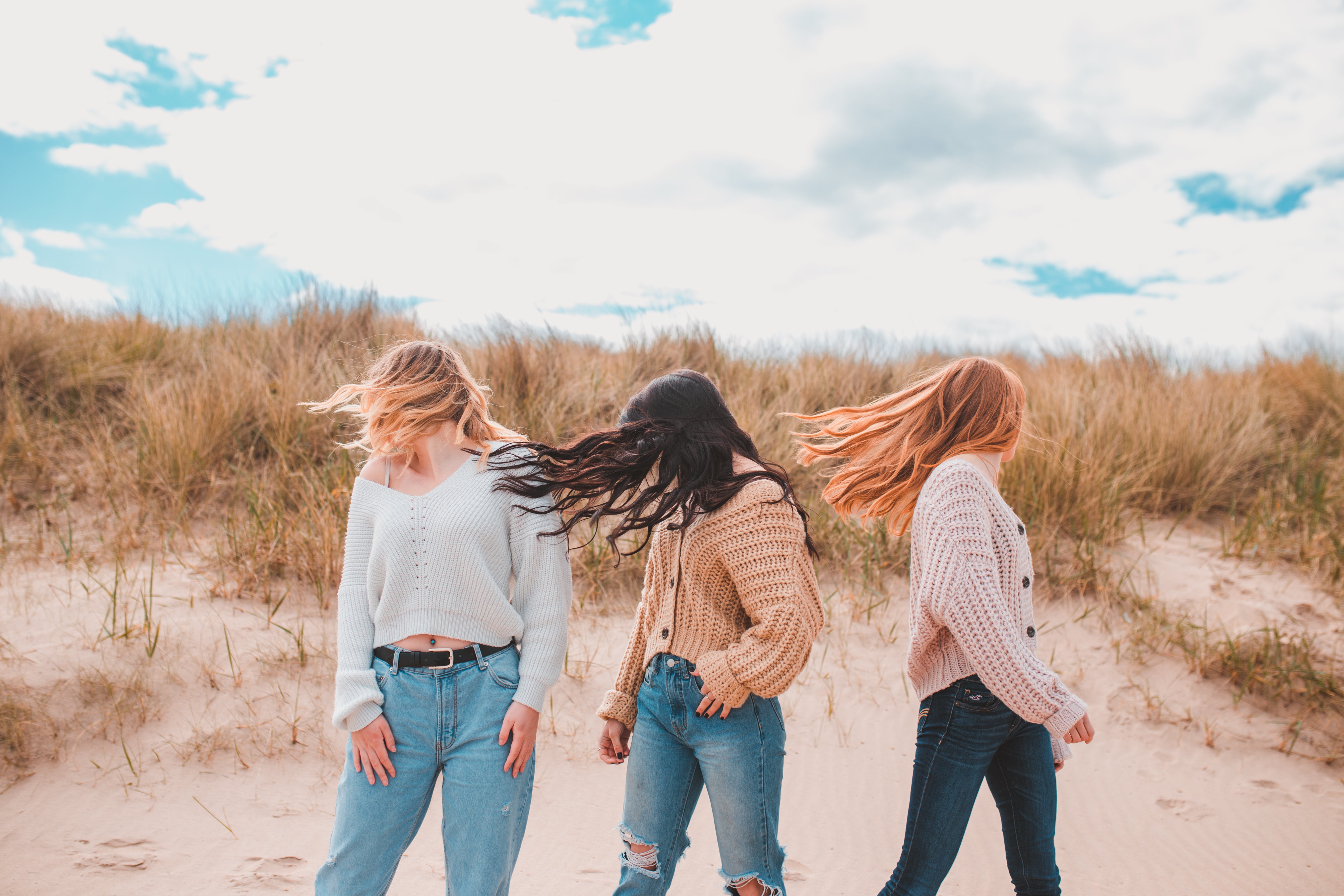 Three girls on the beach, shaking their heads letting their long, luscious hair flow in the wind.