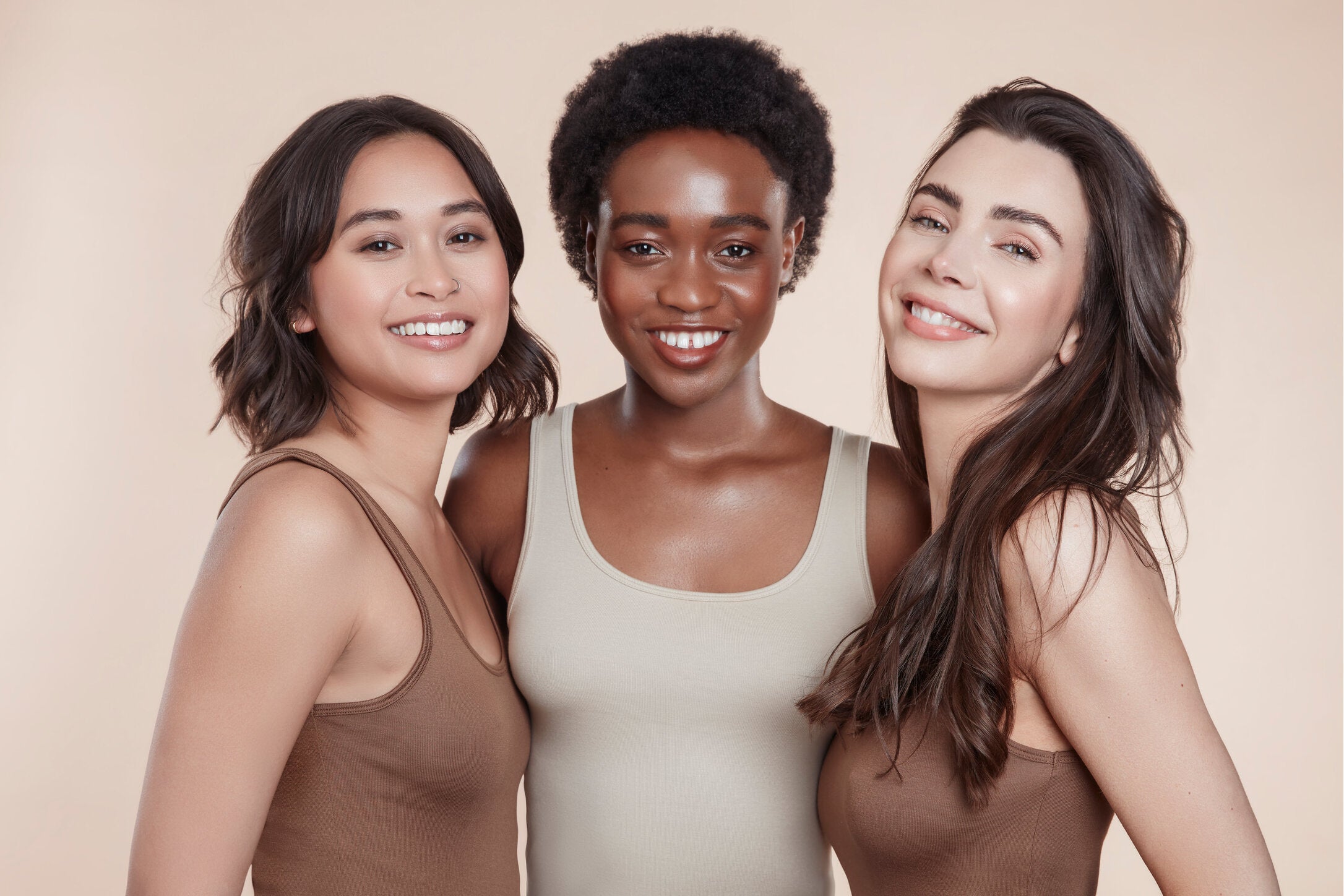 Three female models are smiling at the camera. The model on the left has a short, wavy, brown bob. The model in the middle has short afro hair. The model on the right has long, flowing brown hair.