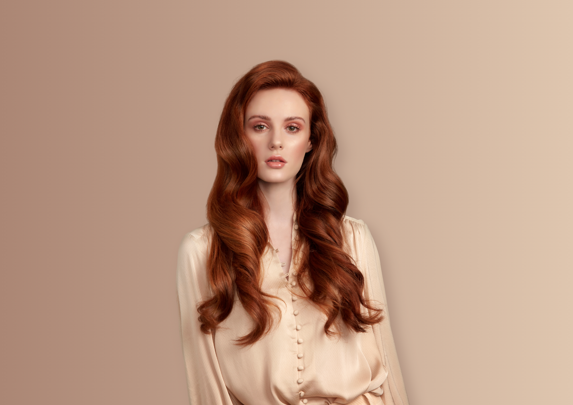 Female model with long, glossy red hair posing in front of a beige background.