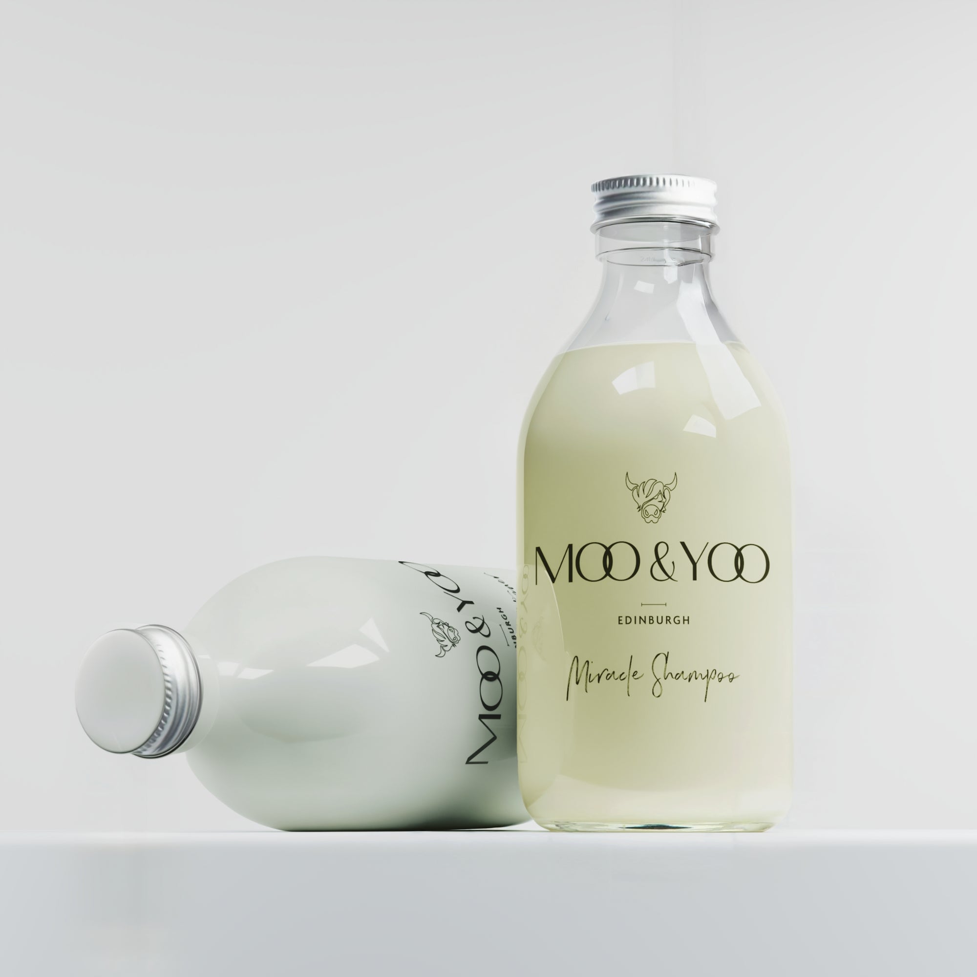 Duo bundle of glass  miracle shampoo bottle standing and the conditioner lying down diagonally behind against a white background