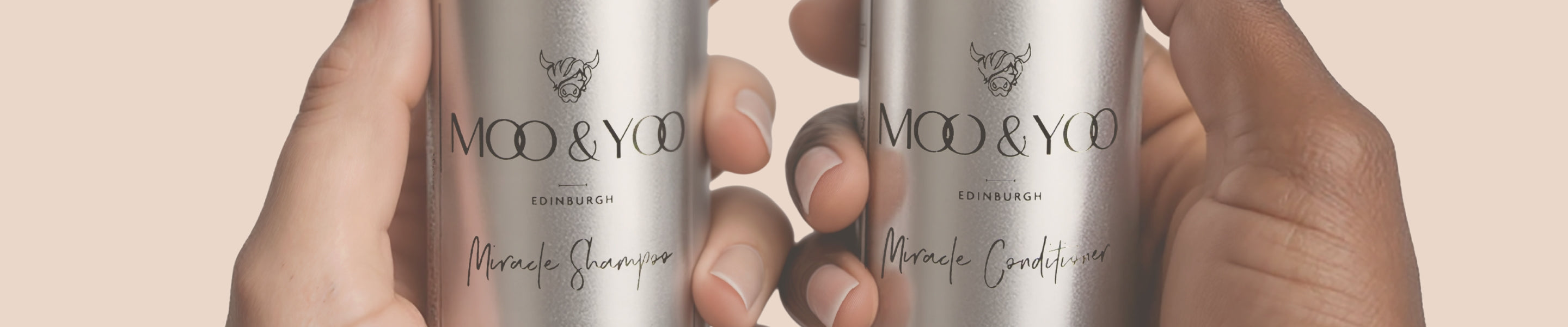 Two bottles of Moo & Yoo shampoo and conditioner in aluminium mini travel bottles held by hands against a beige background