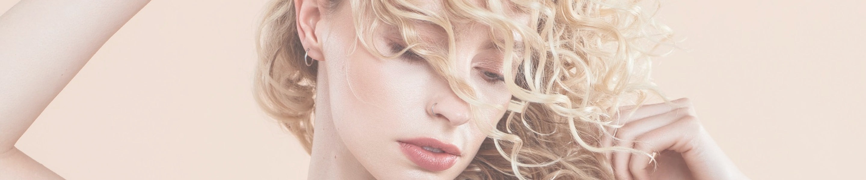 Close-up of a person with blonde curly hair swept across her face against a beige background