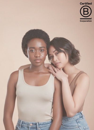 girl on left facing the camera with cropped black afro textured hair, girl on right leaning on her shoulder also facing the camera with short choppy wavy brown hair