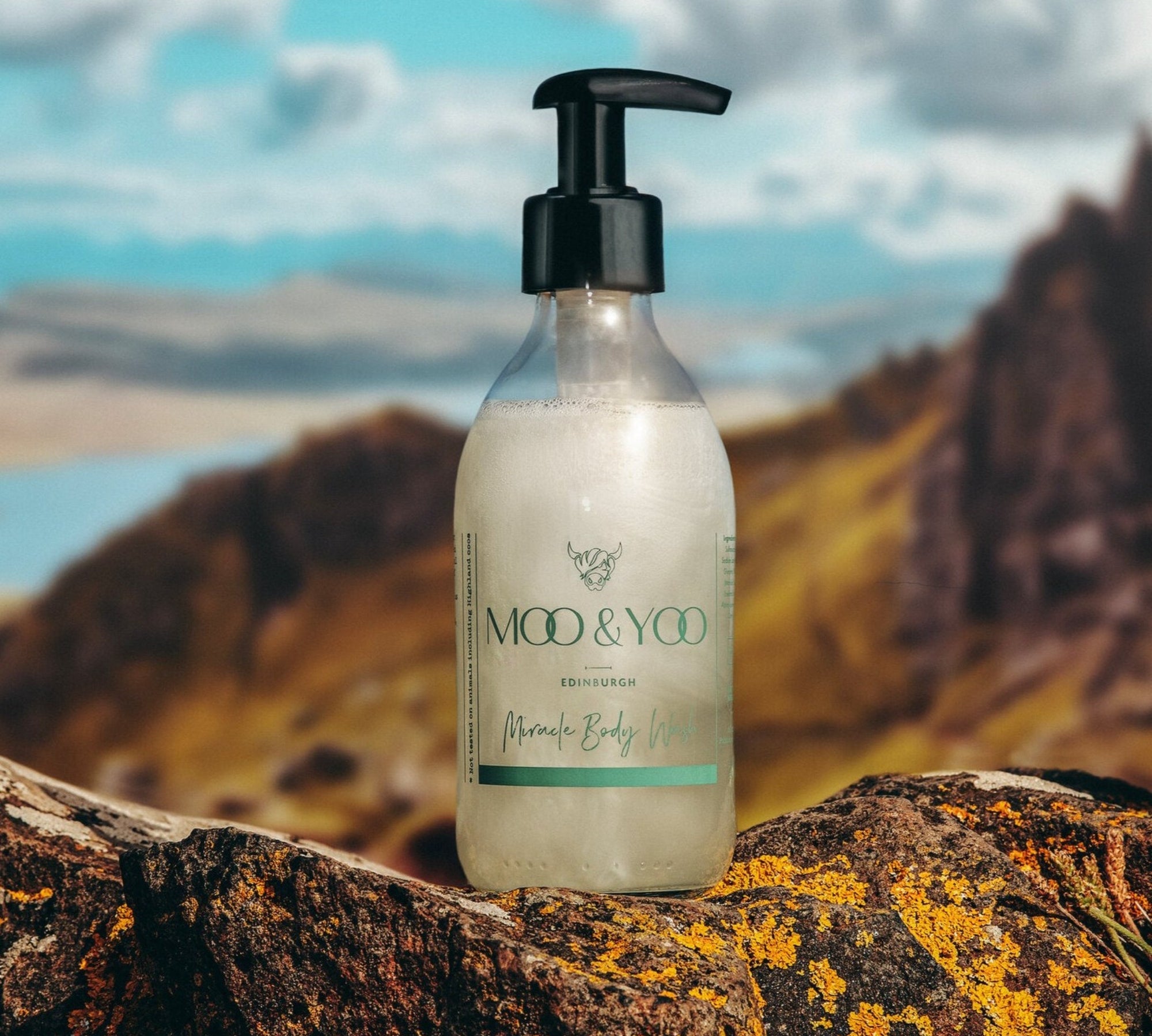 Glass Bottle of Moo and Yoo Body Wash on a rock on top of a Scottish hill overlooking a loch