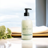 Glass bottle of moo and yoo body wash in a hotel room on a white table with some greenery to one side