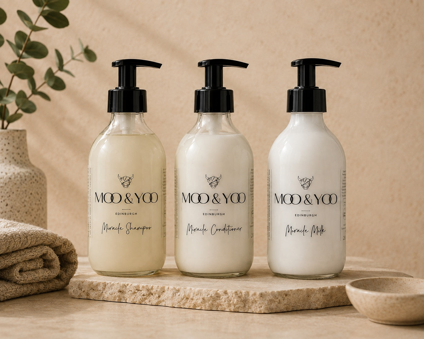 Moo & Yoo luxury haircare bundle featuring Miracle Shampoo, Miracle Conditioner and Miracle Milk in reusable glass bottles on a natural stone tray