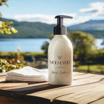 A close up image of a glass bottle of Moo and Yoo Miracle conditioner with a pump. It is placed on a bench overlooking a Scottish loch. There is a small towel to the side. It’s a sunny day with some cloud.