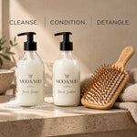Two clear pump bottles of MOO & YOO haircare products, labeled Mo & Yoo Shampoo and Moo & Yoo Conditioner, displayed on a stone surface next to a wooden bamboo paddle hairbrush and a towel. Text at the top reads 'CLEANSE. CONDITION. DETANGLE.